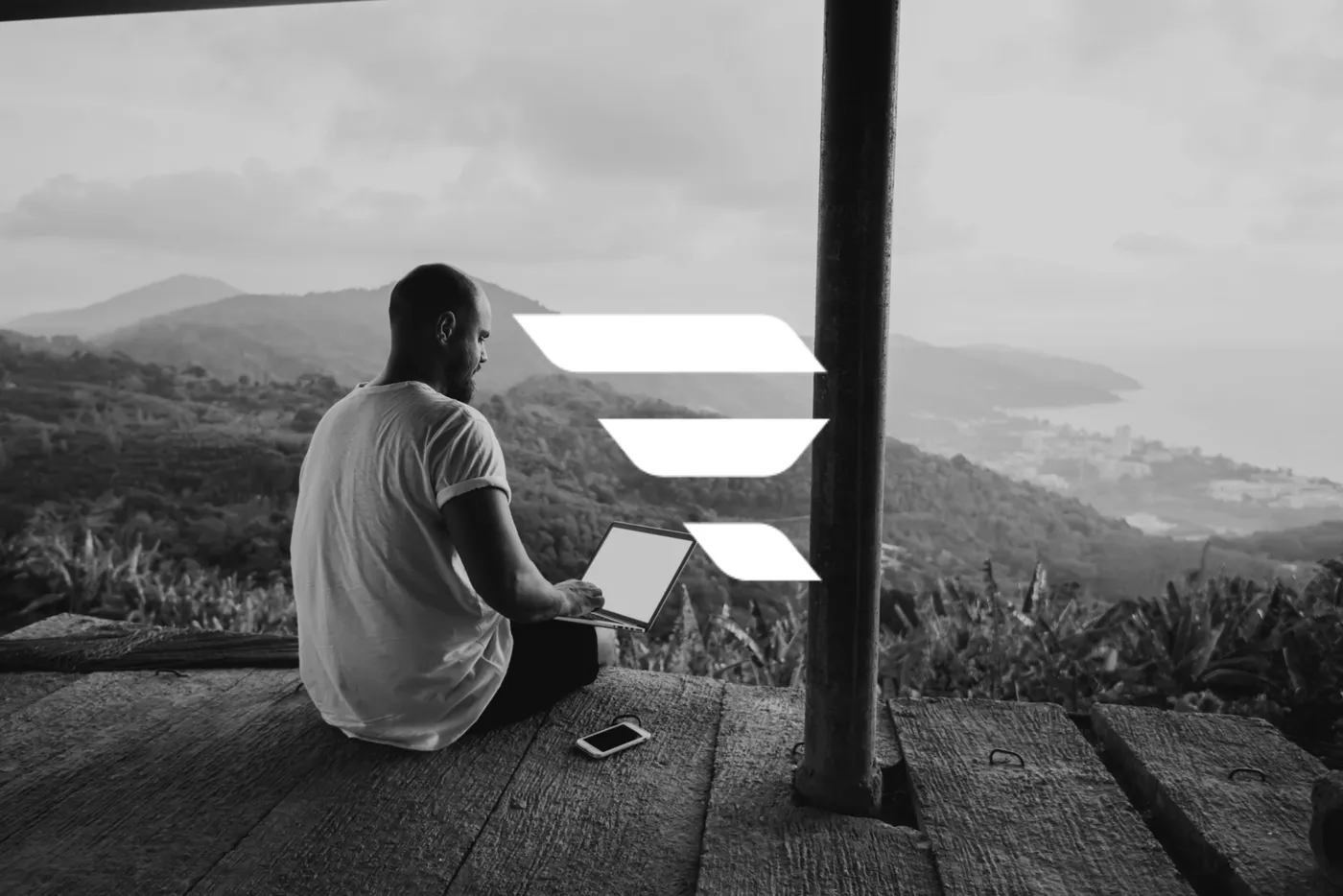 A man working on a laptop on a wooden terrace overlooking a coastal landscape