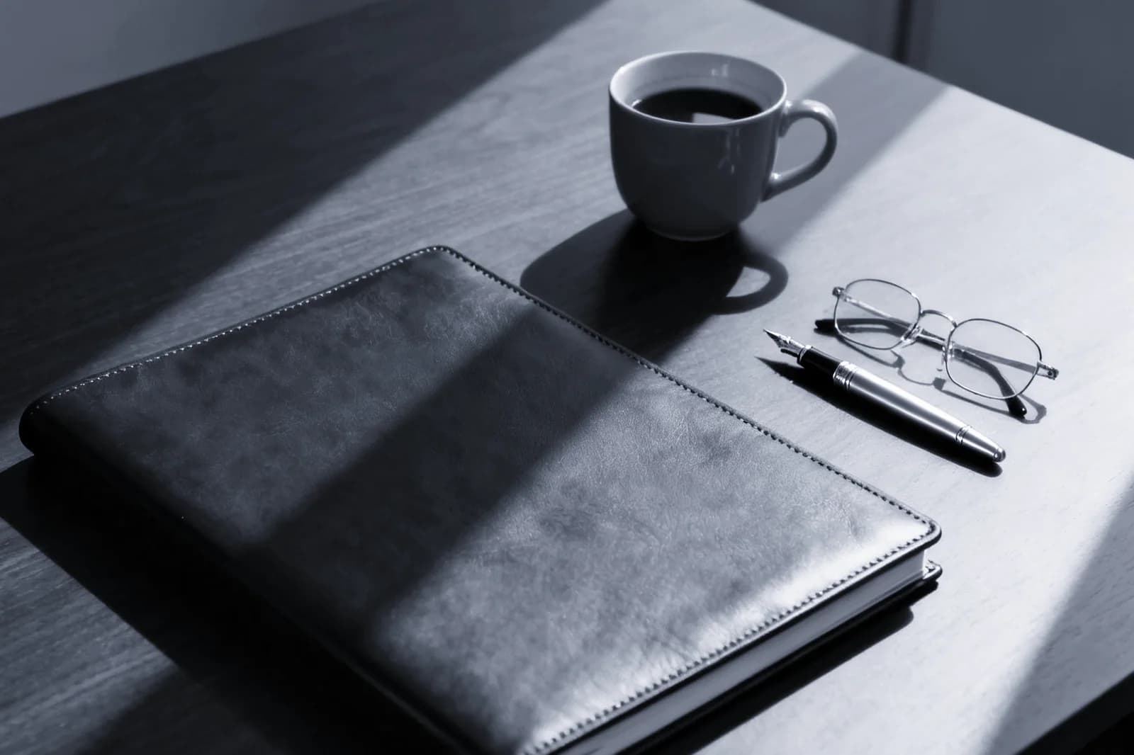 Un escritorio con una carpeta de cuero, una pluma y unos lentes de lectura